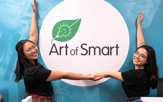 Two Art of Smart tutors smiling at the camera beside the Art of Smart logo